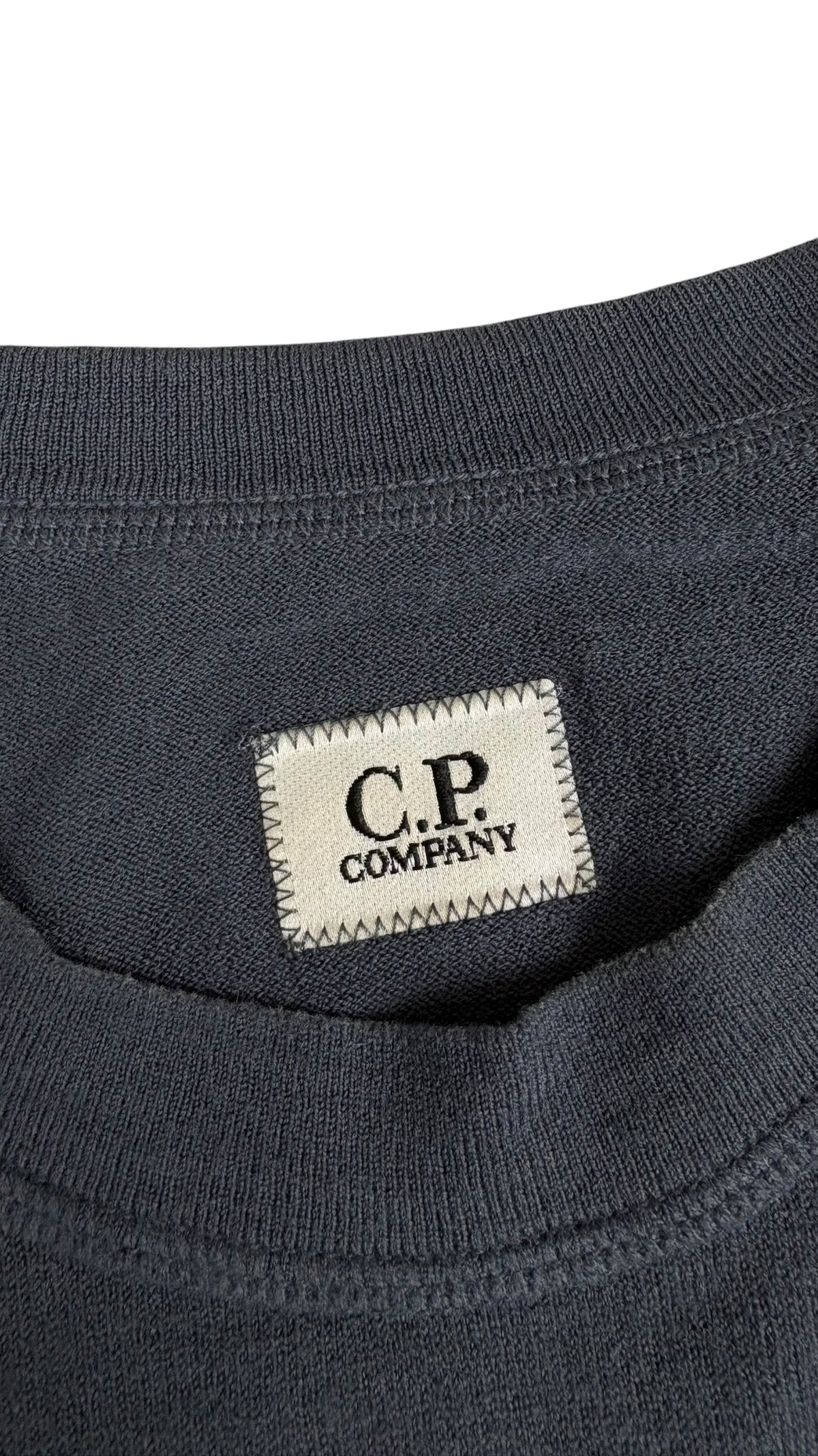 Gros plan sur l'etiquette tissee beige C.P Company cousue sur la poitrine du sweat bleu marine, vue detail
