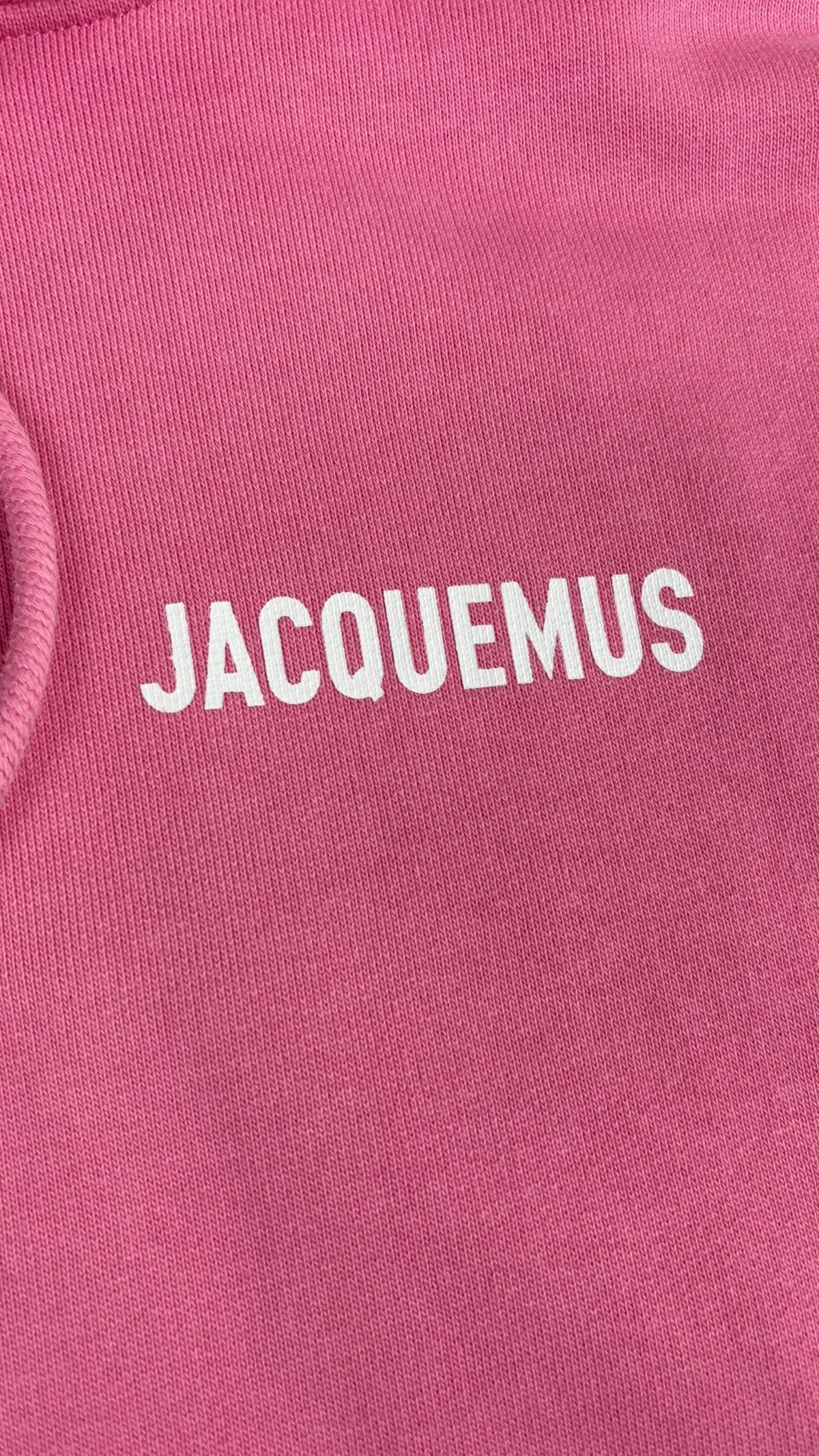 Gros plan du logo Jacquemus blanc floqué sur la poitrine du hoodie rose