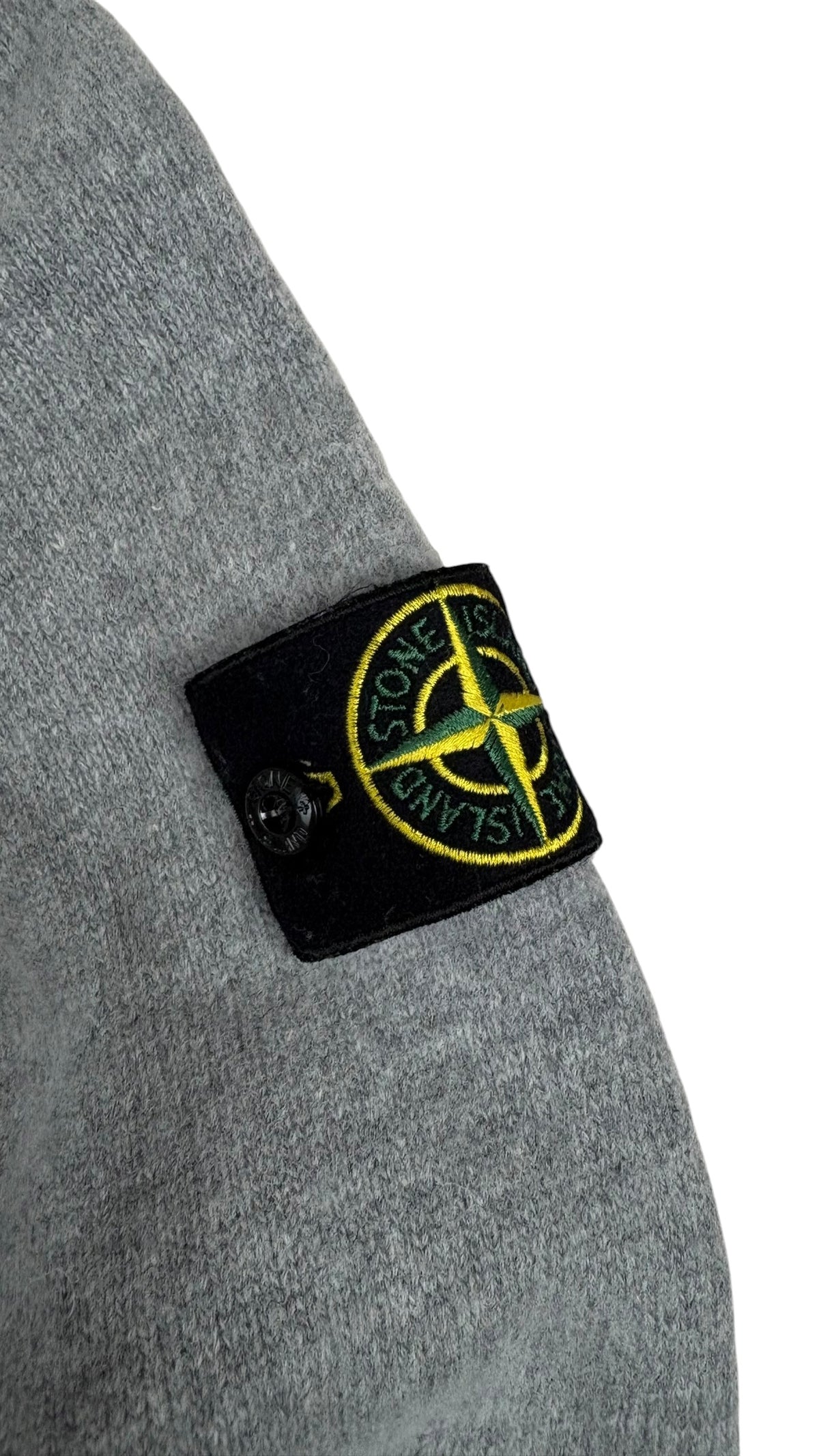 Gros plan du badge boussole Stone Island fixé sur la manche gauche du pull gris