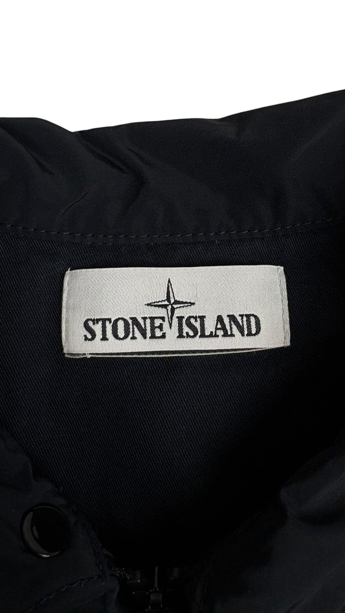 Gros plan sur l'étiquette de marque Stone Island tissée blanche avec le logo boussole, cousue à l'intérieur de la veste bleu marine, vue détail